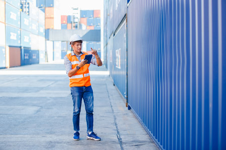 Foreman in uniform wearing safety helmet using tablet checking containers loading. Area logistics import export and shipping cargo freight ship.の写真素材