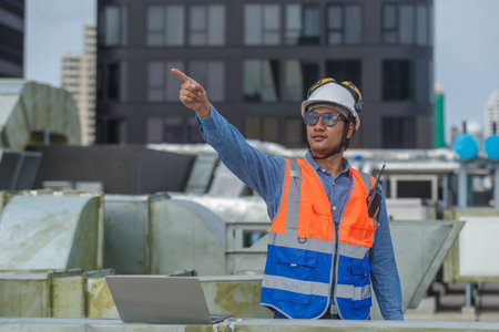 Man Industrial engineer with walkie talkie pointing work at rooftop construction. Male technician working checking HVAC system building factory. Installing large air conditioning system.の写真素材