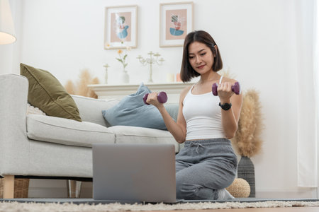 Asian young woman morning exercises hand up holding dumbbell at home, Relax and stretch and workout at home in holiday. Activity body movement arm.の写真素材