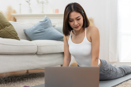 young asian female arm shoulder stretching practicing yoga with laptop sitting on floor in living room at home. Relax and stretch and workout morning at home. Activity body movement exercises.の写真素材