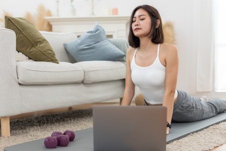 young asian female arm shoulder stretching practicing yoga with laptop sitting on floor in living room at home. Relax and stretch and workout morning at home. Activity body movement exercises.の写真素材