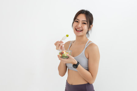 Asian attractive lady sportswear healthy eating salad vegetables over white background. Female holding salad bowl various vegetables and fruit healthy food for weight loss and exercise.の写真素材