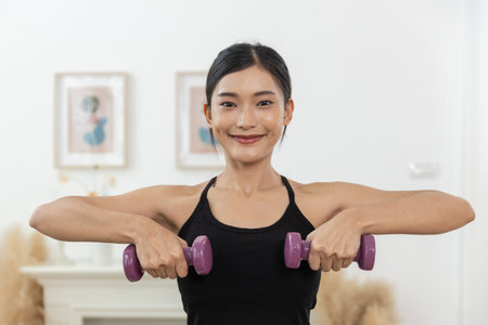 women with dark hair engages in a workout routine using purple dumbbells in room. She appears cheerful and focused, promoting a healthy lifestyle.の写真素材
