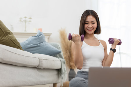 young female working out shoulder holding up dumbbell active strong exercising arm training online looking laptop muscle fitness weight.の写真素材