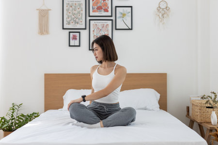 Asian young woman morning exercises after waking up on bed, Stretch feet forward. Relax and stretch and workout at home in holiday. Activity body movement.の写真素材