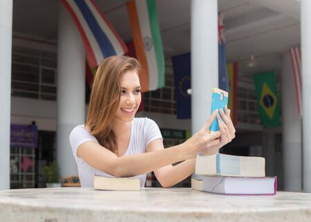 Asian women students Using a mobile phone while reading a book. on campus.の写真素材