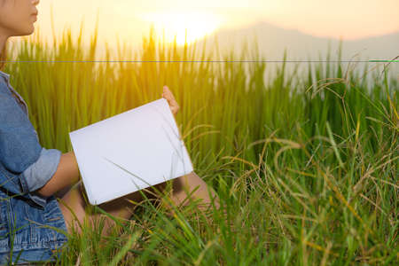 young woman sit reading book at meadows.の写真素材