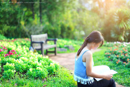 Relaxed young beautiful woman reading a book at theflower garden with sun shining.の写真素材