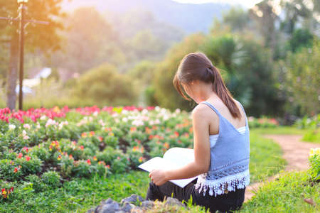 Attractive student Asia girl sitting on pink floral field and read book, doing homework outdoors,education conceptの写真素材