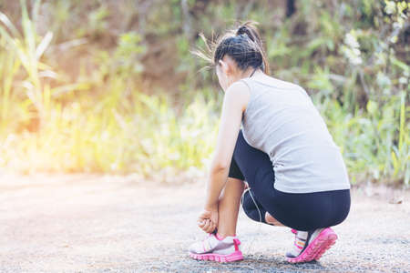 Asia woman runner jogging exercise alone to lose fat weight tying shoelacesの写真素材