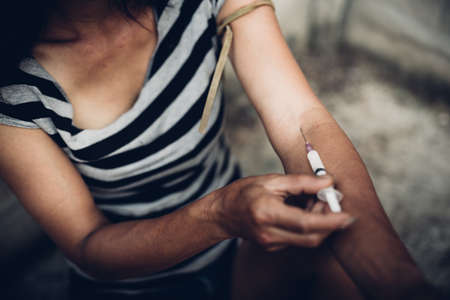 Drug addict young woman with syringe in action, Drug abuse concept.の写真素材
