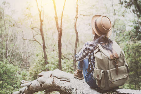 Girl traveler with a backpack sits on logs in the forest.の写真素材