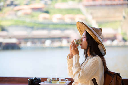 Female tourists are sitting and sipping tea by the reservoir and smiling happily.