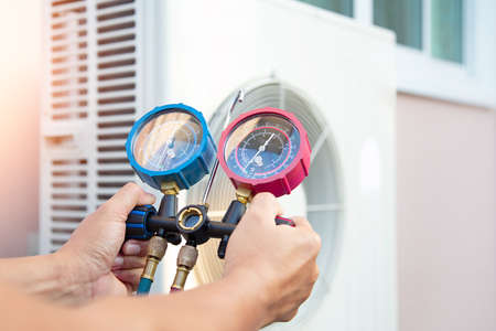 Hands of Technician are using a measuring tool to check Vacuum pump evacuates air for air conditioner.の写真素材