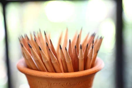 Many pencils that have been used In a jar made of natural materials against a glass window...