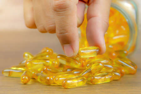 Hand choose a cod liver oil  capsule from a pile of cod liver oil or fish oil dietary supplement for...