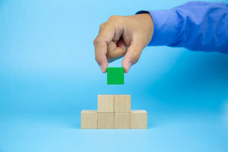 Hand picking a cube shape wooden block toy stacked without graphics for Business design concept and activity for child foundation practice skills.の写真素材