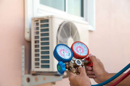 Mechanic air repair using manifold gauge for filling home air conditioner and checking maintenance outdoor air compressor unit.の写真素材
