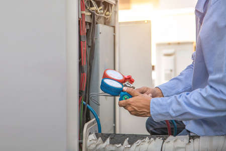 Technician using manifold gauge is measuring equipment for filling industrial factory air conditioners and checking maintenance outdoor air compressor unit.