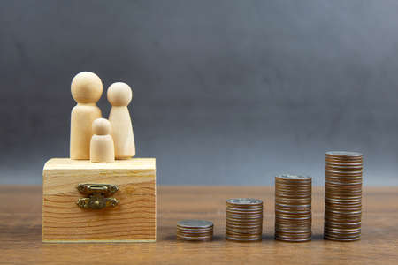 Many coins are stacked in a graph shape with family wooden doll for money saving ideas and financial...