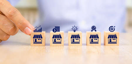 Close-up hand choose cube wooden toy blocks place in line up with franchise business store icon. for small business growth and  branch expansion strategy of financial marketing planning.の写真素材