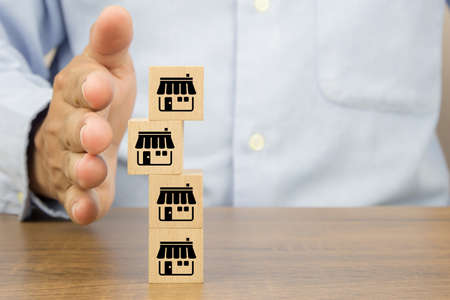 Close-up hand and cube wooden toy blocks stacked with franchise business store icon. for small business growth and branch expansion strategy of financial marketing planning.の写真素材