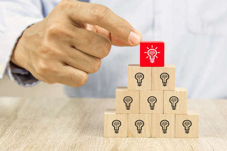 Close up hand choosing light bulb or lamp icons on cube wooden toy blocks concepts human resources...