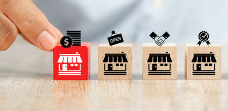 Close-up hand choose cube wooden toy blocks place in line up with franchise business store icon. for small business growth and  branch expansion strategy of financial marketing planning.の写真素材