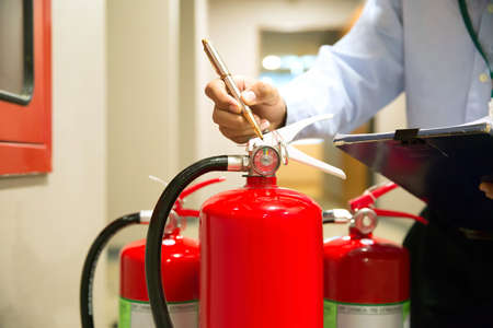 Fire fighter are checking pressure gauge of red fire extinguishers tank in the buildingの写真素材