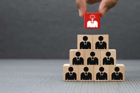 Close up hand choosing people icons with a light bulb on cube wooden toy blocks concepts of idea human resources for business organizations and leadership.の写真素材