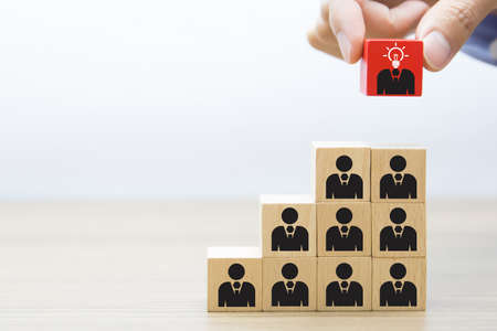 Close up hand choosing people icons with a light bulb on cube wooden toy blocks concepts of idea human resources for business organizations and leadership.の写真素材