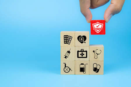 Hand choose medical icon on cube wooden toy blocks stack in with other medical symbols concepts of illness treatment and health safety insurance.の写真素材