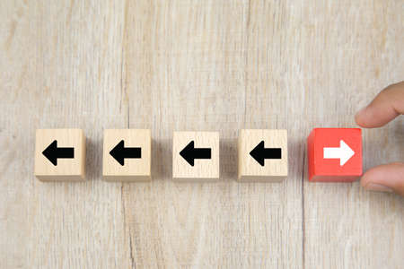Businessman hand chooses cube wooden toy block with arrow head icons pointing to opposite directions for business leader of the change to growth and success concepts.の写真素材