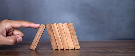 Close-up fingers prevent the wooden block from falling domino concepts of financial risk management...
