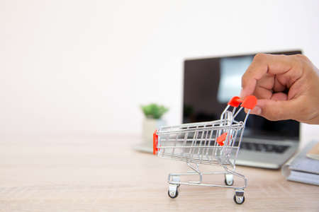 Close up hands pushing the shopping cart on desk with computer laptop background concept of using the application for online spending and shopping at home.の写真素材