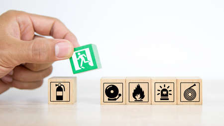 Close-up hand choose a wooden toy blocks stacked with fire exit icon for fire safety protection concepts.の写真素材