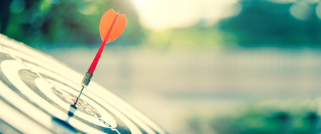 Close-up the bullseye target or dart board has red dart arrow throw hitting the center of a shooting with the sun shines and shadows for business targeting and winning goals business conceptsの写真素材