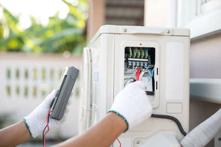 Close up technician hand using measuring equipment checking electric current voltage at circuit breaker on outdoor air compressor unit after installation and air conditioner services maintenanceの写真素材