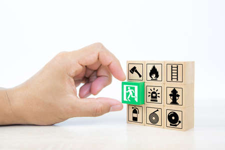 Close-up hand choose wooden toy blocks stacked with door exit sing icon with fire extinguisher and...