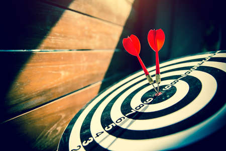 Close-up the bullseye target or dart board has red dart arrow throw hitting the center of a shooting with the sun shines and shadows for business targeting and winning goals business conceptsの写真素材
