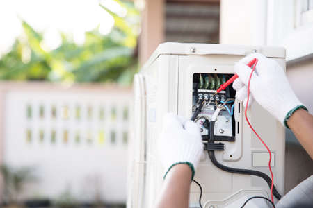Close up technician hand using measuring equipment checking electric current voltage at circuit breaker on outdoor air compressor unit after installation and air conditioner services maintenanceの写真素材