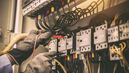Close-up hand of electrical engineering using measuring equipment tool to checking electricity at circuit breaker and cable wiring system for maintenance in main power distribution board.の写真素材