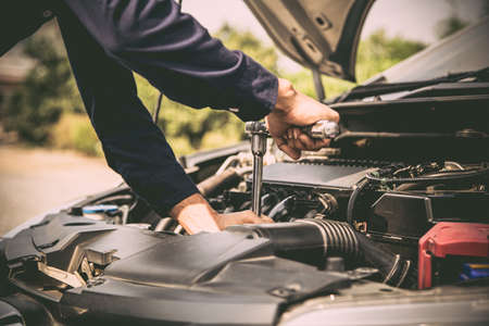 Close-up hands of auto mechanic are using the wrench to repair and maintenance auto engine is problems at car repair shop. Concepts of car care check and fixed and services insurance.の写真素材