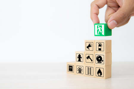 Close-up hand choose wooden toy blocks stacked with door exit sing icon with fire extinguisher and fire protection symbol for safety prevent and protect accident of emergency and rescue.の写真素材