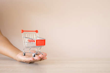 Close up the shopping cart on hand on desk concept of using the internet application for online shopping buying and spending on smartphone.の写真素材