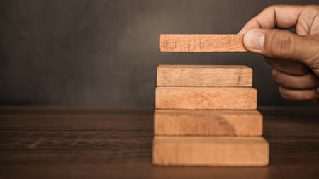 Close-up hand is placing wood block tower stacked in pyramid shape with caution to prevent collapse...