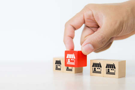 Hand choose cube wooden toy blocks stacked with franchise business store icon for growth and strategy of financial marketing planning and bank loan for branch expansion franchisee.の写真素材