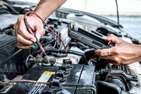 Close up hand of auto mechanic using measuring equipment tool checking car battery. Concepts of fix and checking for repair service and old car maintenance and insurance.の写真素材