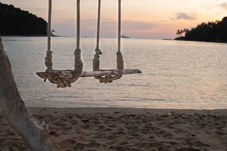 Wooden swing hang under a tree sand and sea beach on the backgroundの写真素材