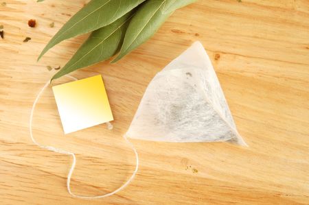 Fresh leaves and pyramidion tea bag on wooden boardの写真素材